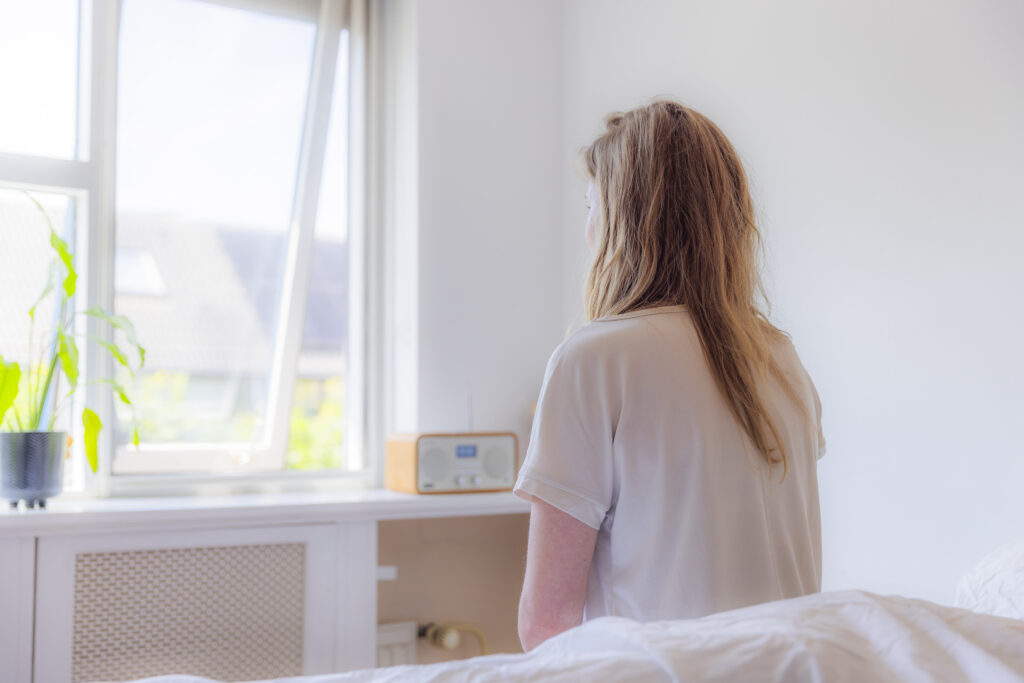 foto van vrouw die op bed zit en naar buiten kijkt